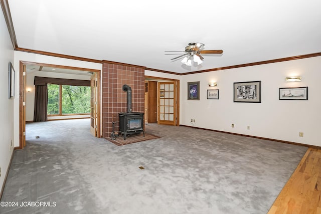 unfurnished living room with carpet flooring, a wood stove, ceiling fan, and ornamental molding