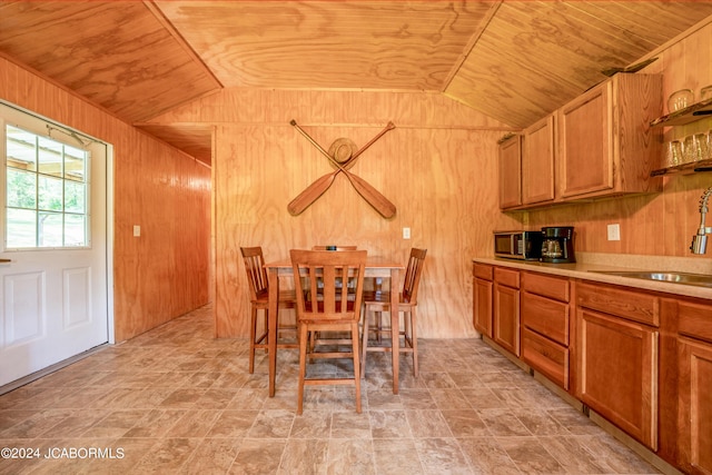 dining space featuring lofted ceiling, wood walls, wood ceiling, and sink