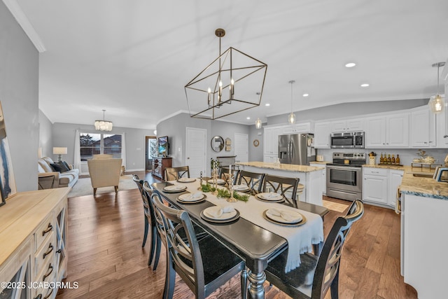 dining area with a notable chandelier, wood-type flooring, ornamental molding, and vaulted ceiling