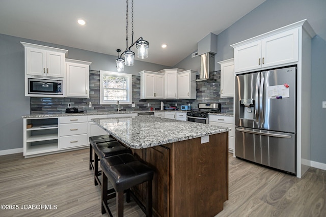 kitchen featuring a kitchen island, appliances with stainless steel finishes, white cabinetry, a kitchen breakfast bar, and wall chimney exhaust hood