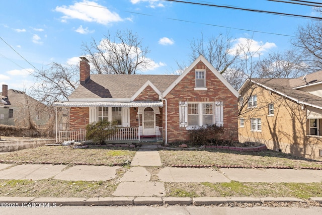 view of front of home featuring brick siding, a front lawn, a porch, roof with shingles, and a chimney