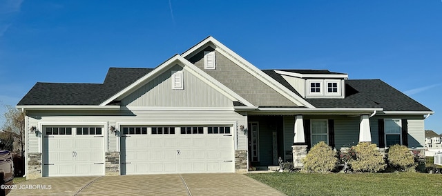 craftsman-style home featuring a shingled roof, concrete driveway, stone siding, an attached garage, and a front yard