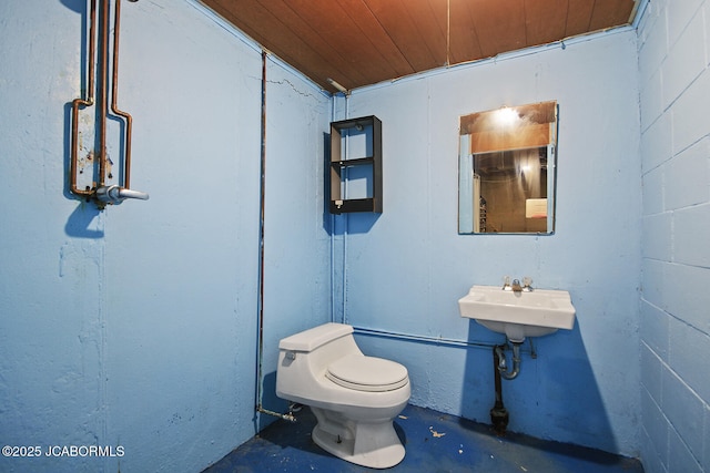 half bathroom with a sink, wooden ceiling, concrete flooring, and toilet