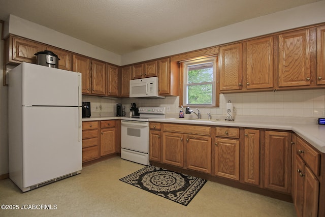 kitchen with brown cabinetry, a sink, backsplash, and white appliances