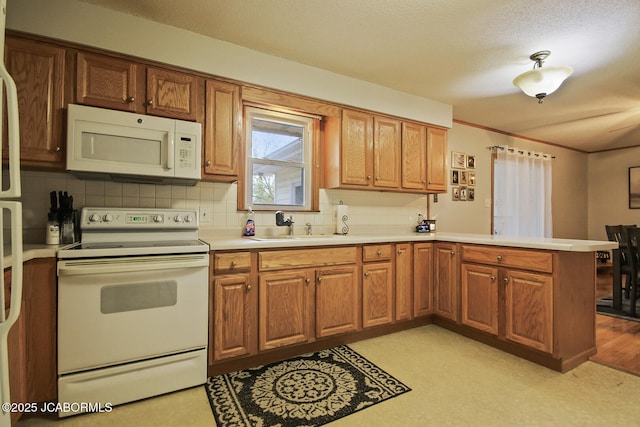 kitchen with a peninsula, white appliances, light countertops, tasteful backsplash, and a sink