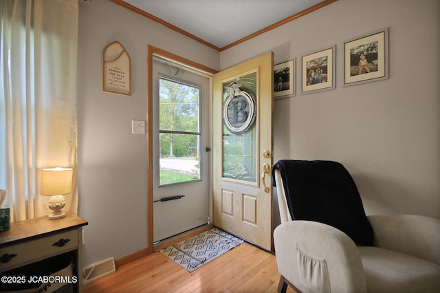 doorway with visible vents, baseboards, crown molding, and light wood-type flooring