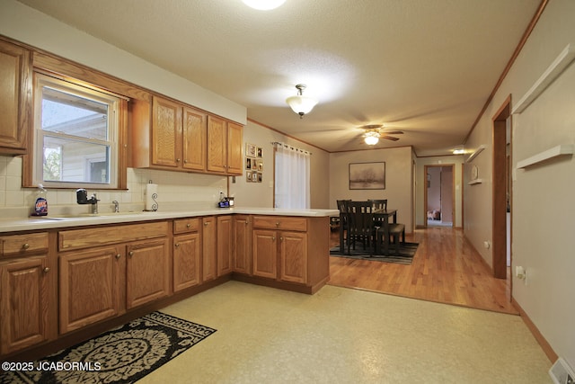 kitchen with backsplash, a ceiling fan, a sink, light countertops, and a peninsula