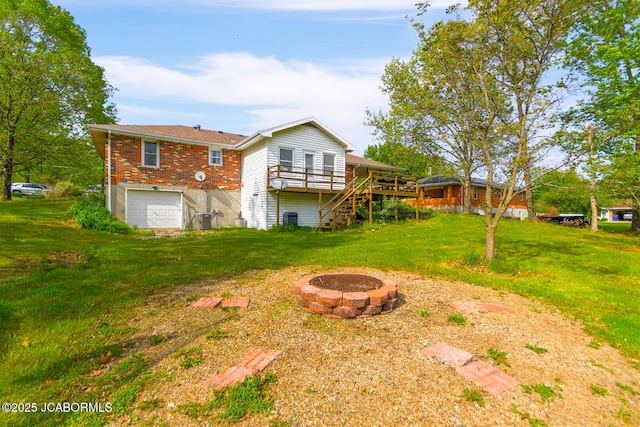 back of house with a garage, a fire pit, a deck, stairs, and a lawn
