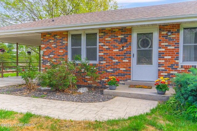 view of exterior entry featuring brick siding and roof with shingles