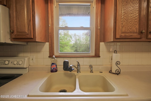 kitchen featuring brown cabinetry, white electric range oven, light countertops, a sink, and backsplash