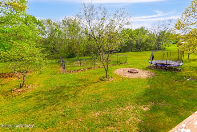 view of yard featuring fence, a trampoline, and an outdoor fire pit