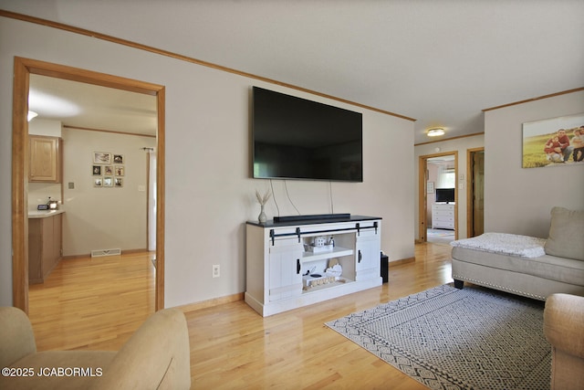 living area with baseboards, ornamental molding, light wood-type flooring, and visible vents