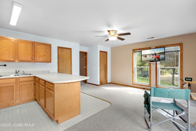 kitchen with light carpet, a sink, light countertops, a peninsula, and a ceiling fan