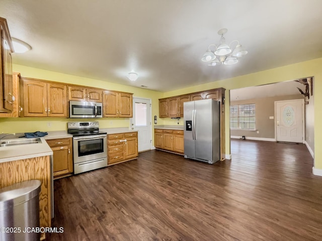 kitchen with dark wood-style flooring, stainless steel appliances, light countertops, a notable chandelier, and a wealth of natural light