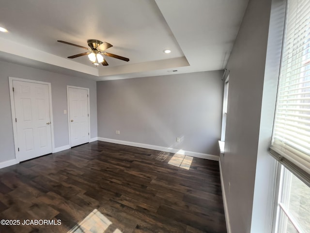 interior space with dark wood-type flooring, baseboards, ceiling fan, recessed lighting, and a raised ceiling