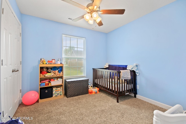 bedroom with carpet floors, visible vents, a ceiling fan, a crib, and baseboards