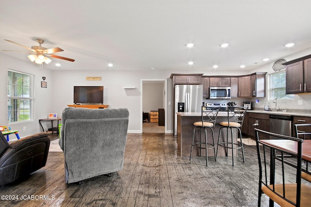 kitchen with open floor plan, appliances with stainless steel finishes, dark brown cabinetry, and a kitchen breakfast bar