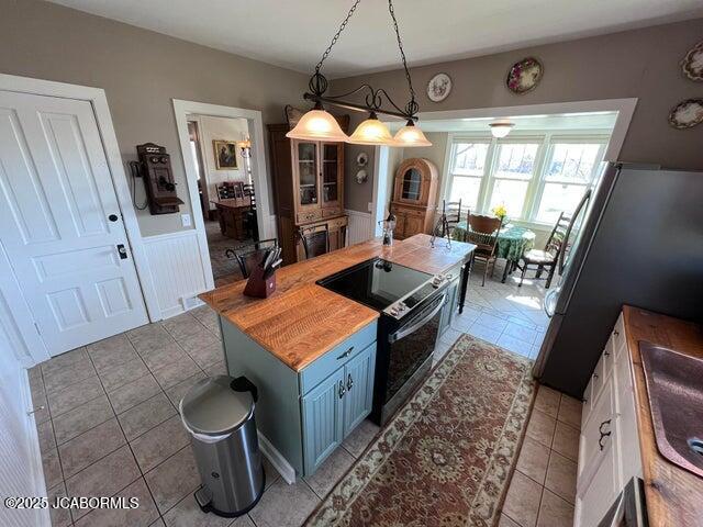 kitchen with electric range oven, light tile patterned floors, blue cabinetry, hanging light fixtures, and wooden counters