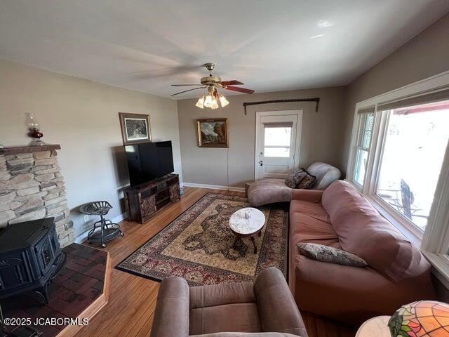 living area with a wood stove, ceiling fan, wood finished floors, and baseboards