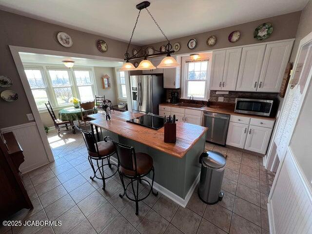 kitchen with appliances with stainless steel finishes, white cabinets, a sink, a kitchen breakfast bar, and tile patterned flooring