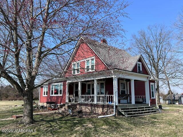 view of front of house featuring covered porch, a chimney, and a front lawn