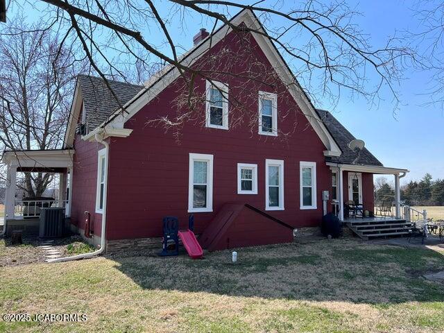 rear view of property with a chimney, a porch, a lawn, and central air condition unit