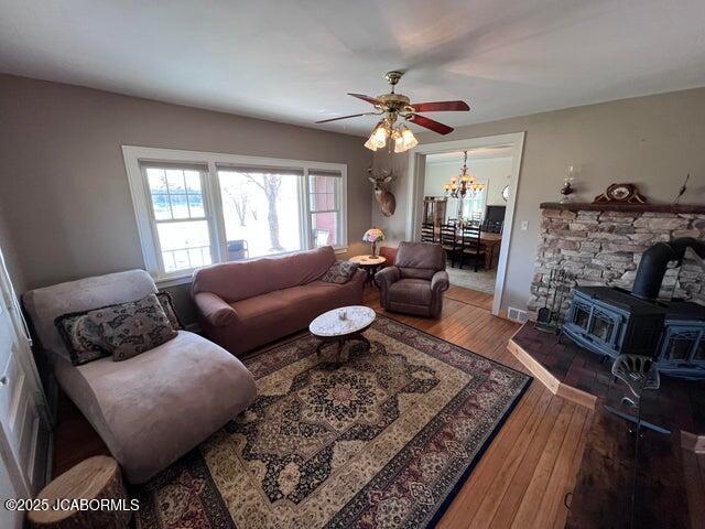 living room with wood-type flooring, a ceiling fan, a wood stove, and a chandelier