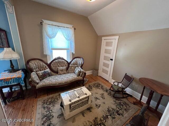 living area featuring wood finished floors, lofted ceiling, and baseboards