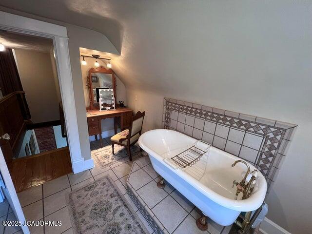 bathroom featuring vaulted ceiling, a soaking tub, tile patterned floors, baseboards, and vanity