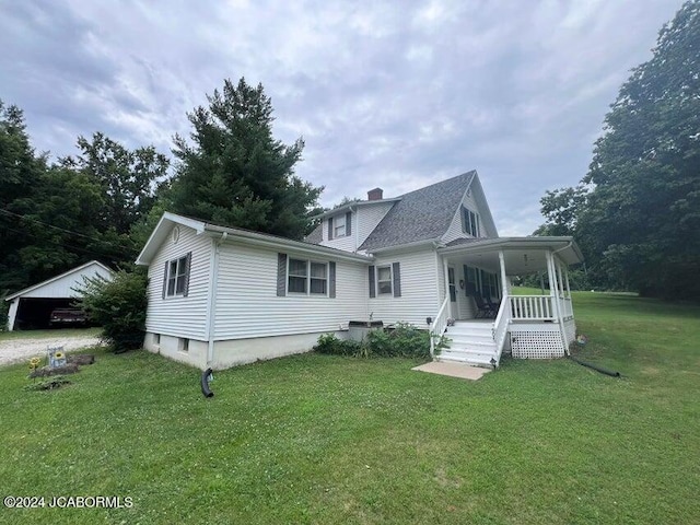 rear view of property featuring a lawn, a garage, covered porch, and an outbuilding