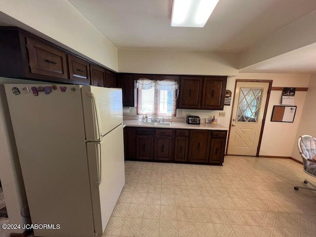 kitchen with white refrigerator, dark brown cabinetry, and sink