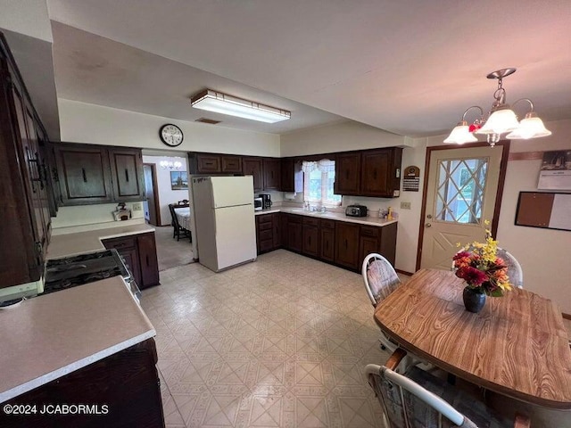 kitchen featuring dark brown cabinetry, range with gas cooktop, an inviting chandelier, white fridge, and hanging light fixtures