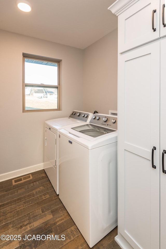 laundry room with cabinet space, visible vents, dark wood-type flooring, washing machine and dryer, and baseboards