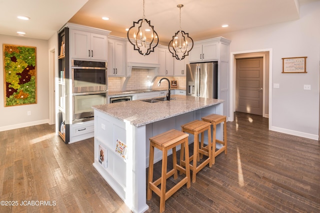 kitchen featuring dark wood-style floors, decorative backsplash, appliances with stainless steel finishes, a kitchen island with sink, and a sink