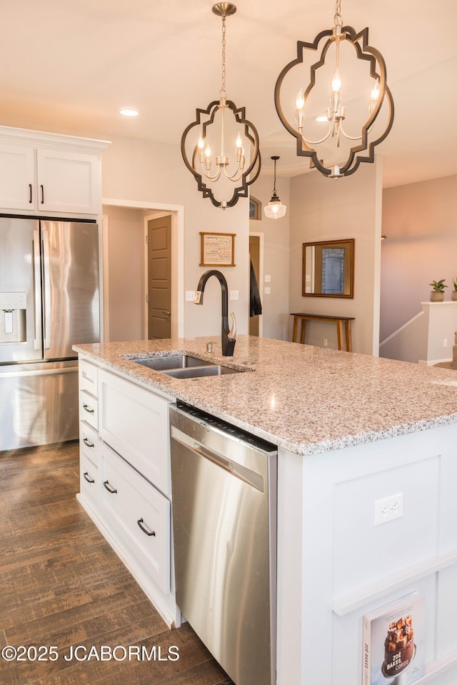 kitchen featuring stainless steel appliances, a sink, light stone counters, and an inviting chandelier