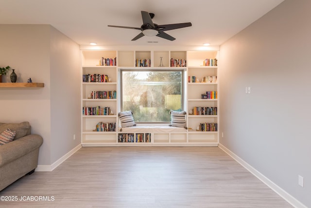 sitting room featuring built in shelves, wood finished floors, a ceiling fan, and baseboards