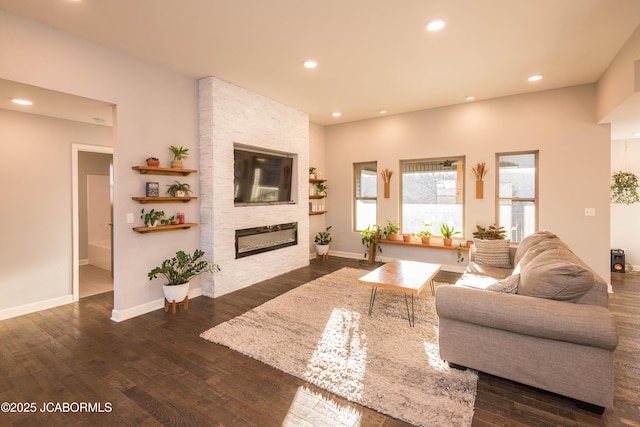 living area with recessed lighting, dark wood finished floors, a stone fireplace, and baseboards