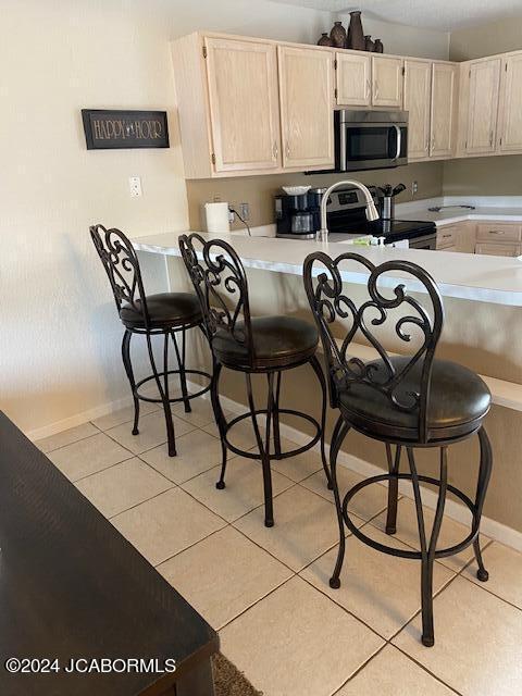 kitchen featuring a breakfast bar, light tile patterned flooring, light brown cabinets, and appliances with stainless steel finishes