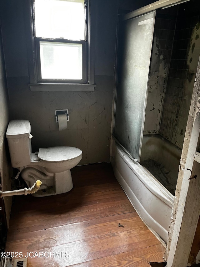 bathroom featuring combined bath / shower with glass door, wood finished floors, and toilet