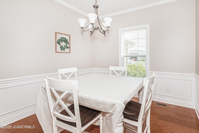 dining room with crown molding, a chandelier, a wainscoted wall, a decorative wall, and wood finished floors