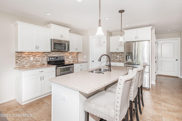 kitchen featuring appliances with stainless steel finishes, a sink, backsplash, a breakfast bar area, and an island with sink