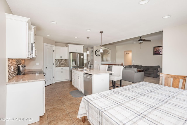 kitchen with stainless steel appliances, decorative backsplash, a ceiling fan, a sink, and a kitchen breakfast bar