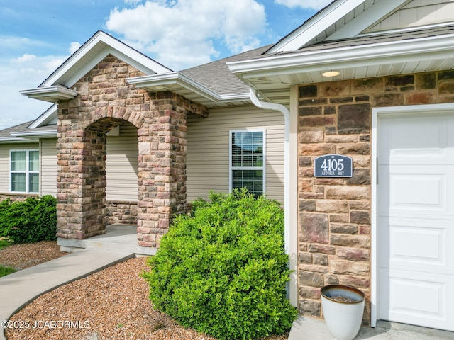 doorway to property with stone siding, a shingled roof, and an attached garage