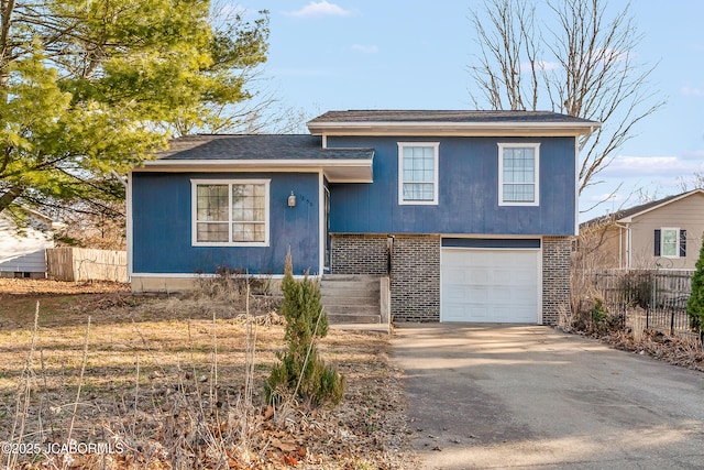 split level home featuring brick siding, concrete driveway, an attached garage, and fence