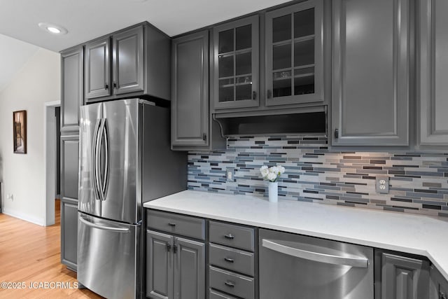 kitchen with gray cabinets, backsplash, appliances with stainless steel finishes, light wood-type flooring, and baseboards