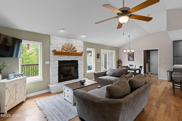 living area featuring a fireplace, light wood-style flooring, ceiling fan with notable chandelier, baseboards, and vaulted ceiling