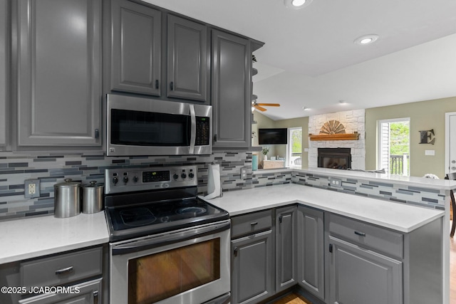 kitchen featuring appliances with stainless steel finishes, tasteful backsplash, a fireplace, gray cabinetry, and a peninsula