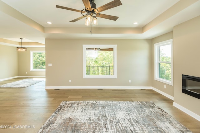 unfurnished living room featuring a raised ceiling, wood-type flooring, and a wealth of natural light