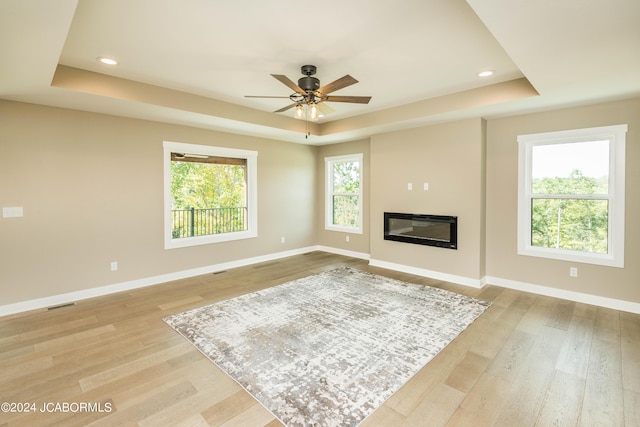 living room featuring a raised ceiling, ceiling fan, and light hardwood / wood-style flooring