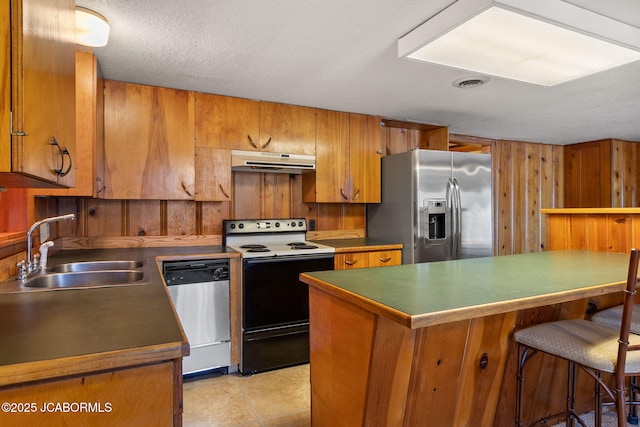 24671 Gardner Rd, Versailles, MO 65084 - kitchen with appliances with stainless steel finishes, a sink, under cabinet range hood, brown cabinets, and wood walls